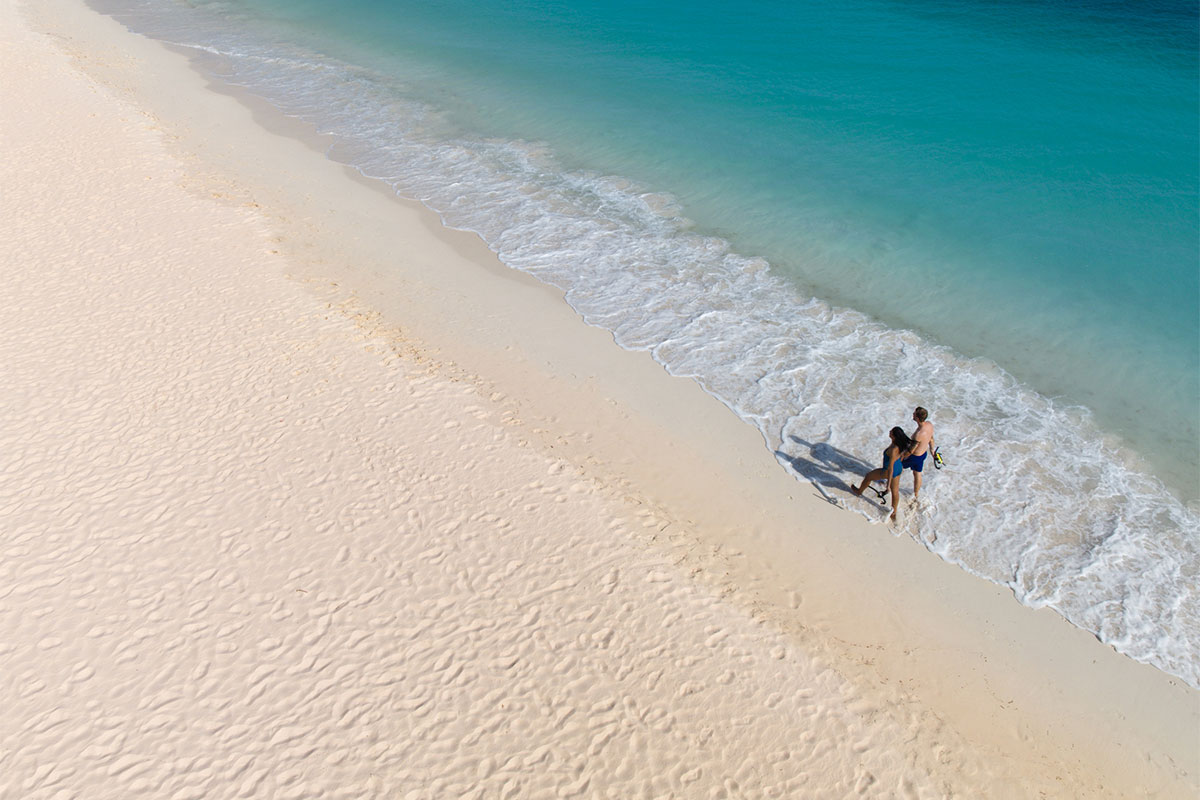Two people walking on the beach with snorkeling gear in hand