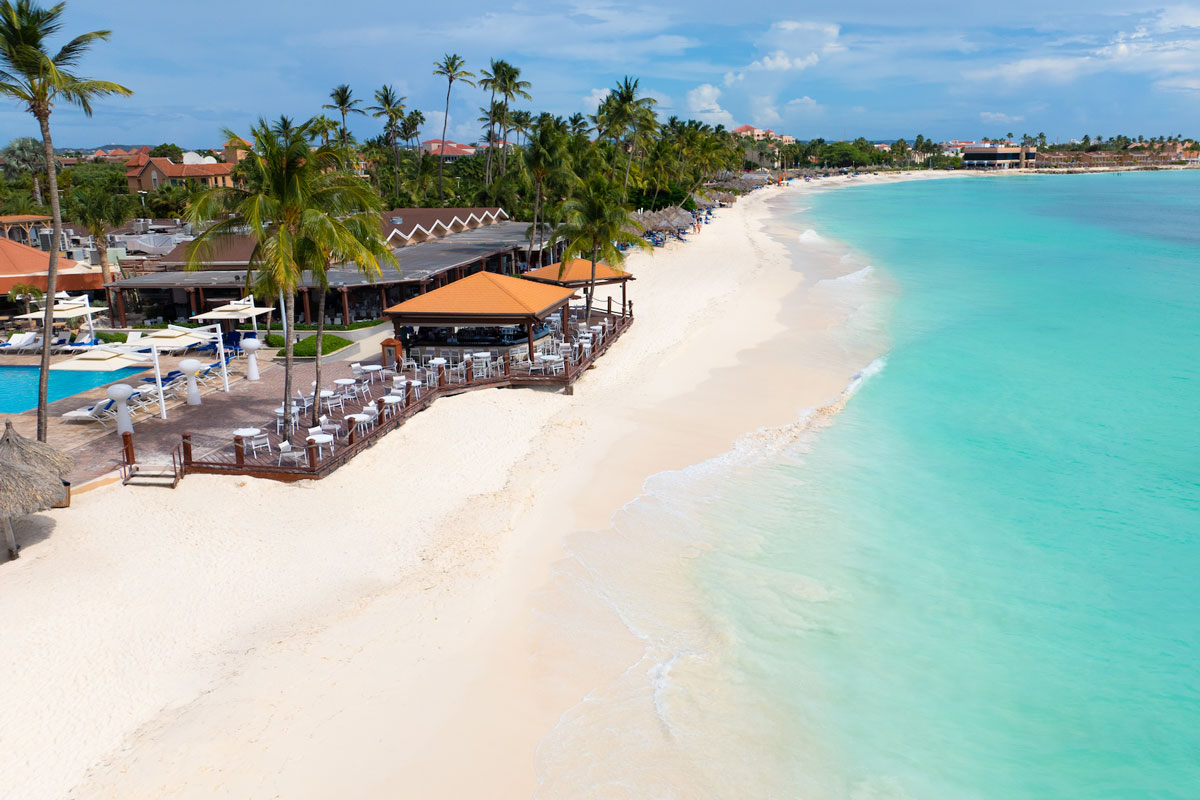 A beach in the caribbean with a boardwalk, pool deck, ad beach bar in view