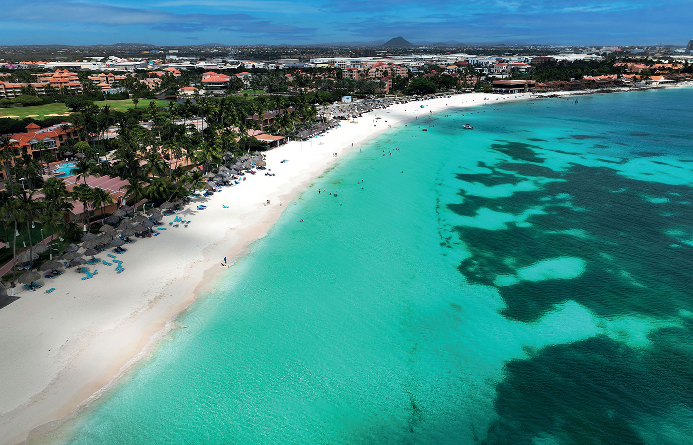 a shoreline of an island with blue water, white sand, and grass huts dotting the shoreline